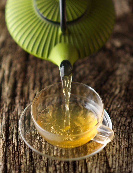 A green Japanese teapot pouring green tea into a glass teacup