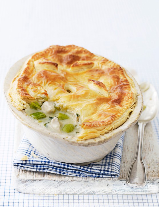 A chicken and leek pie with a golden puff pastry top in a dish with a spoon next to it