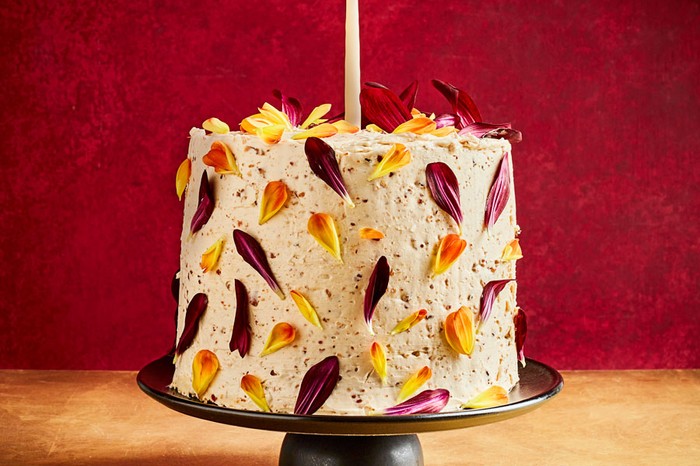 Chocolate and olive oil sponge cake decorated in hazelnut praline and edible flowers on a stand with a candle