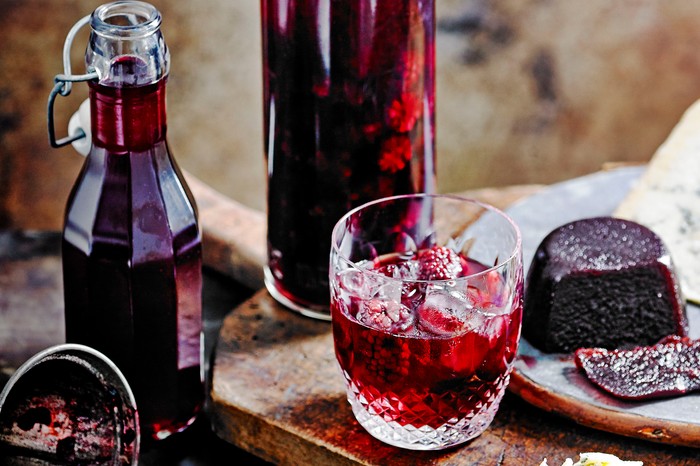 A glass bottle filled with blackberry whisky next to a full glass