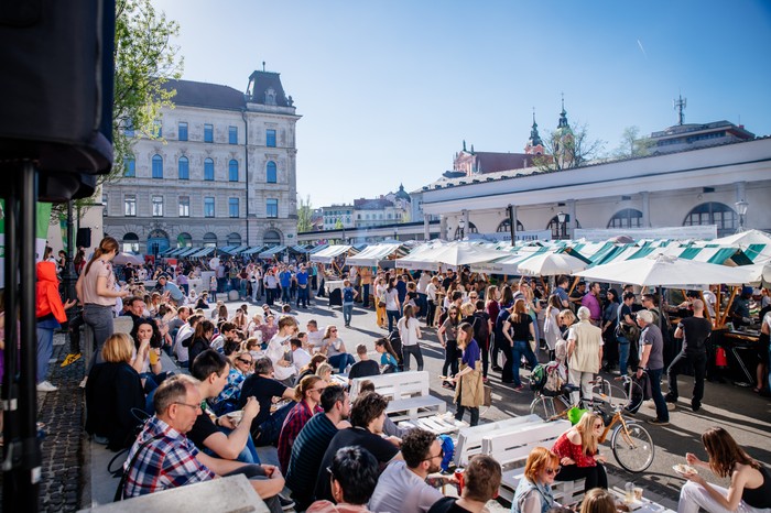 People sat on the pavement by street food stalls at Open Kitchen Market Ljubljana