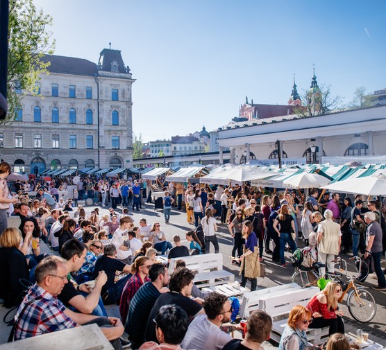 People sat on the pavement by street food stalls at the Open Kitchen Market in Ljubljana