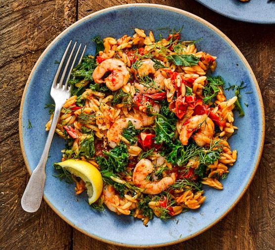 Baked Orzo with Harissa Prawns Baked orzo with harissa prawns on a blue plate with a wedge of lemon and fork