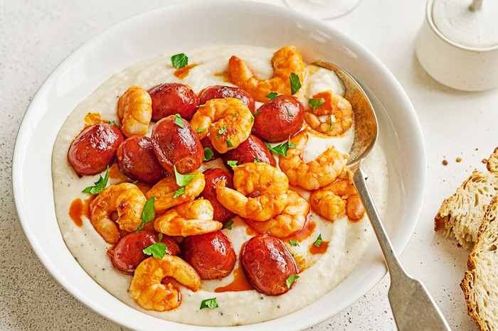 Bowl of white bean dip topped with prawns and mini chorizo sausages