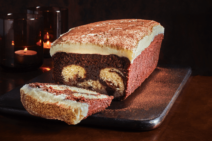 A dark marbled loaf cake topped with cream cheese frosting, with one slice cut out of the end