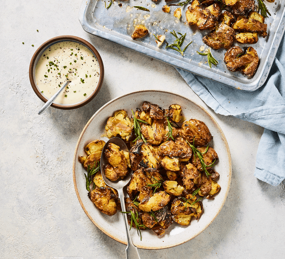 Rosemary roasted smashed new potatoes in a bowl next to mustardy chive aïoli