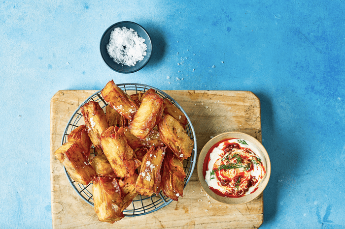 A basket of confit potatoes, next to a dip and pot of salt